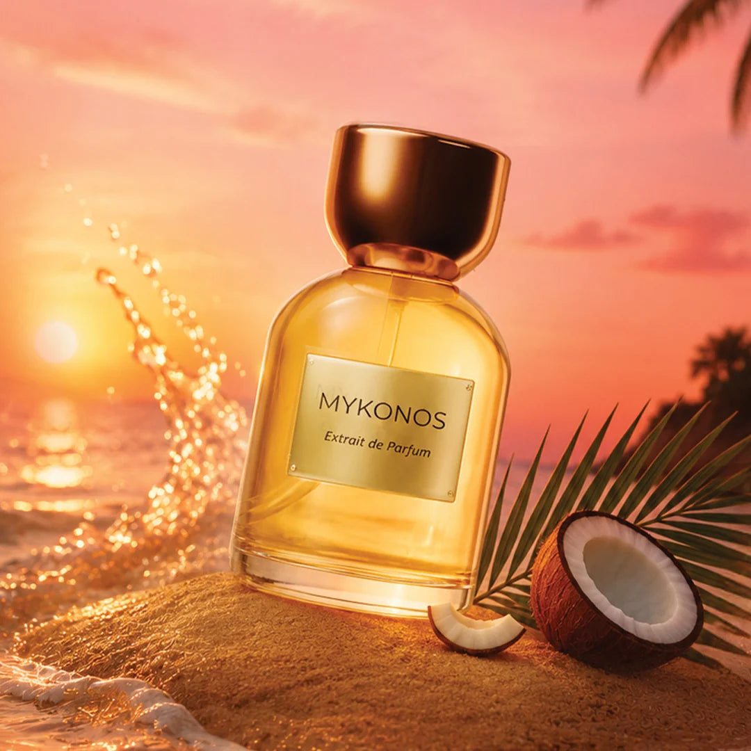 Perfume bottle labeled 'MYKONOS' on sand with sunset and coconut in background